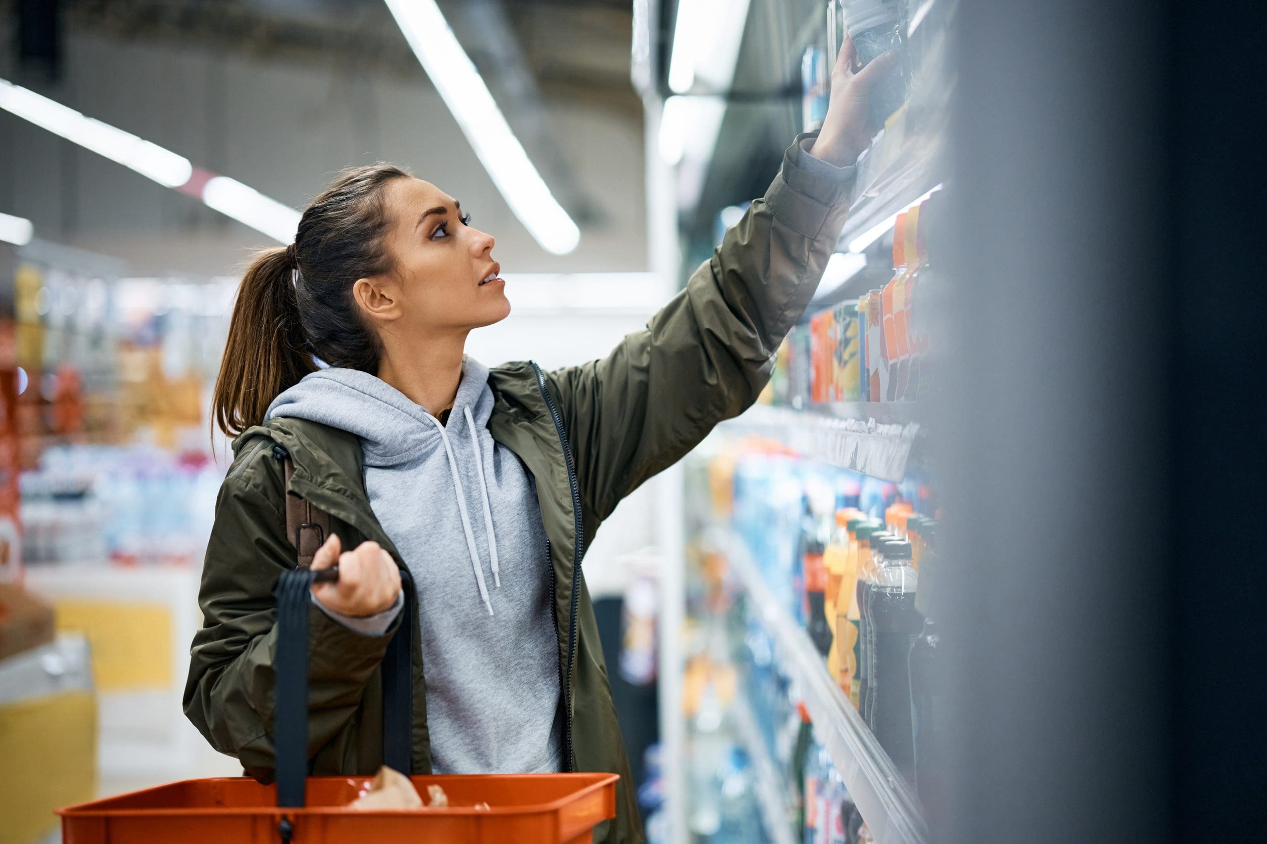 Young woman taking drinks from products shelf while shopping in supermarket.
