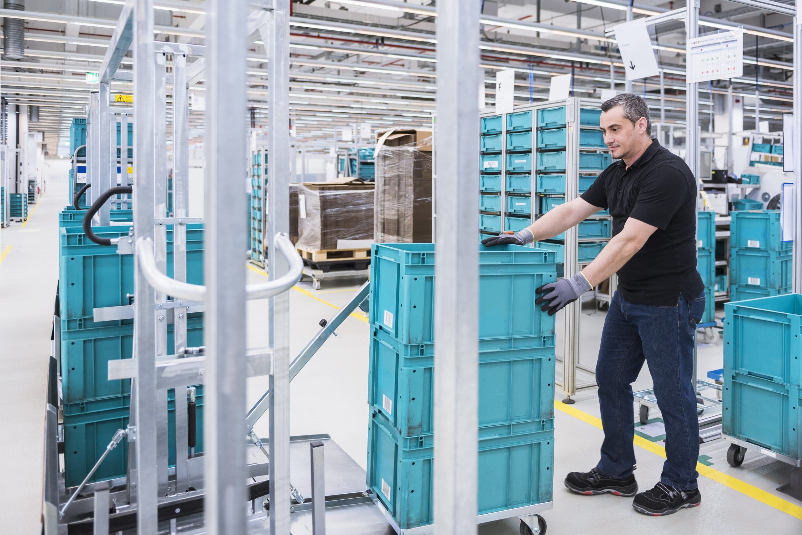 Man at tugger train organising boxes in industrial hall